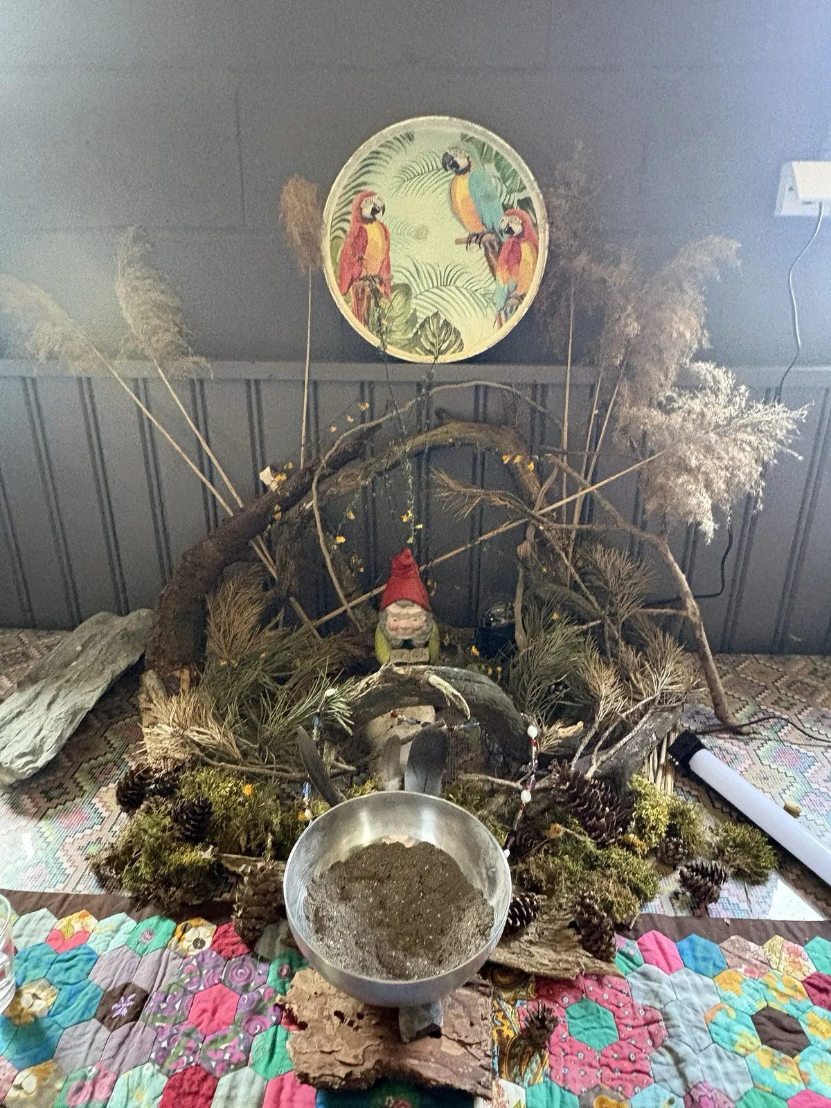 A little altar built from pampas grass, branches and found things, set on a patchwork quilt.