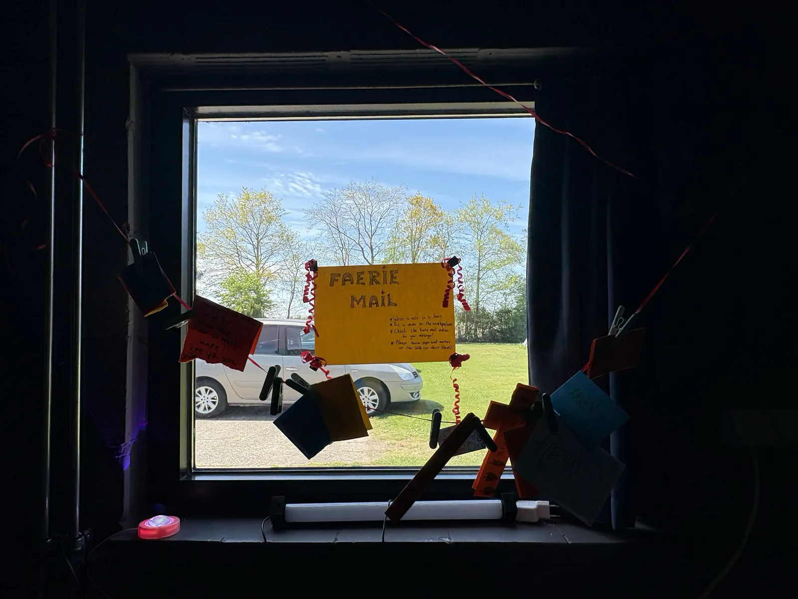 The Faerie Mail post, a hand-lettered sign above rows of paper pockets hanging by a sunlit window.